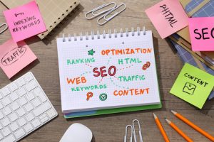 SEO ideas on a notepad. Keyboard, notepads with diagram and stationery on wooden background, top view